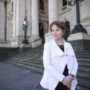 Suzanna on the steps of Parliament House with hands folded looks away from the camera for a side profile picture